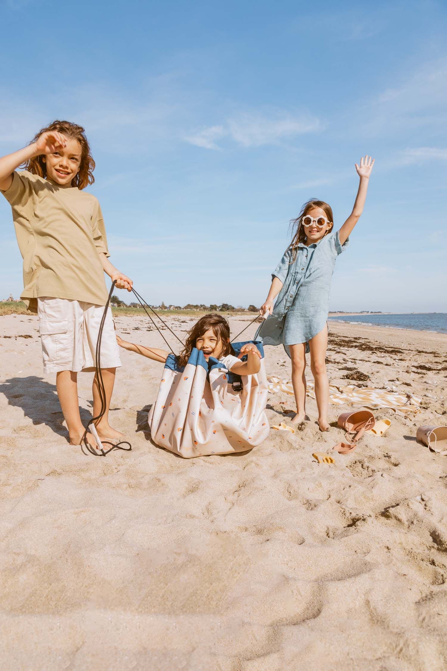 magical days outdoor beach bag, one child is sitting in the closed mat, other children are holding the wrope of the bag