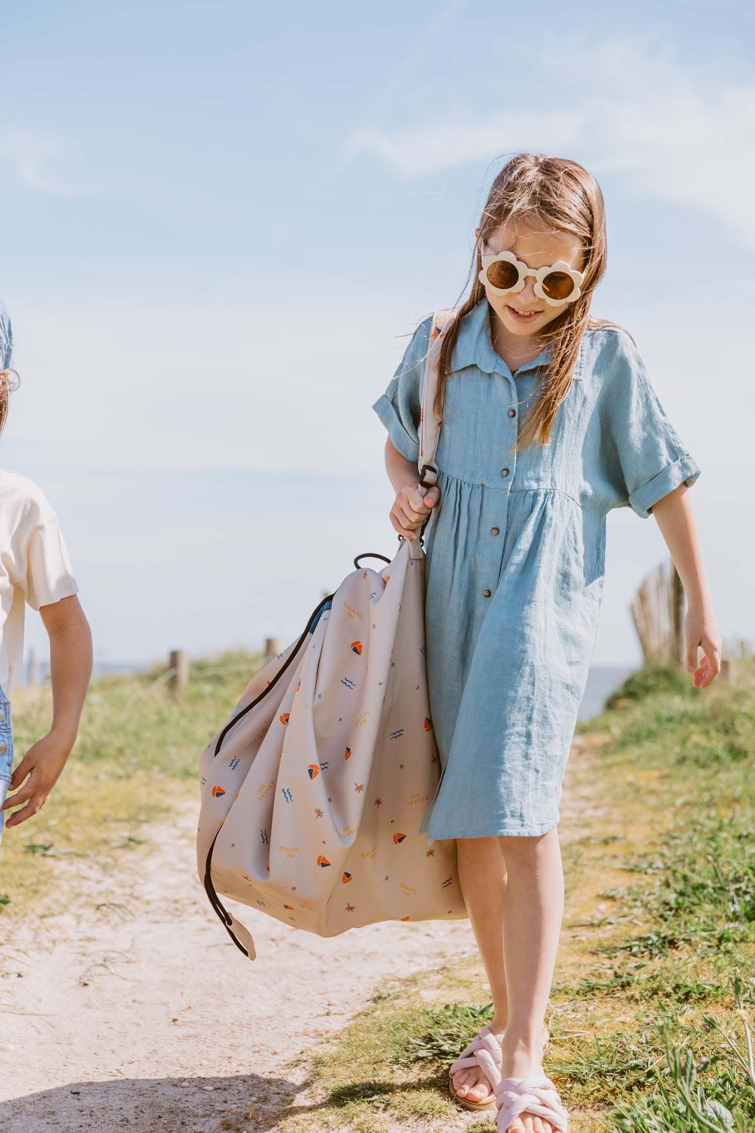 magical days outdoor beach bag, child is carrying the bag on her shoulder by the shoulderstrap, cool sun glasses