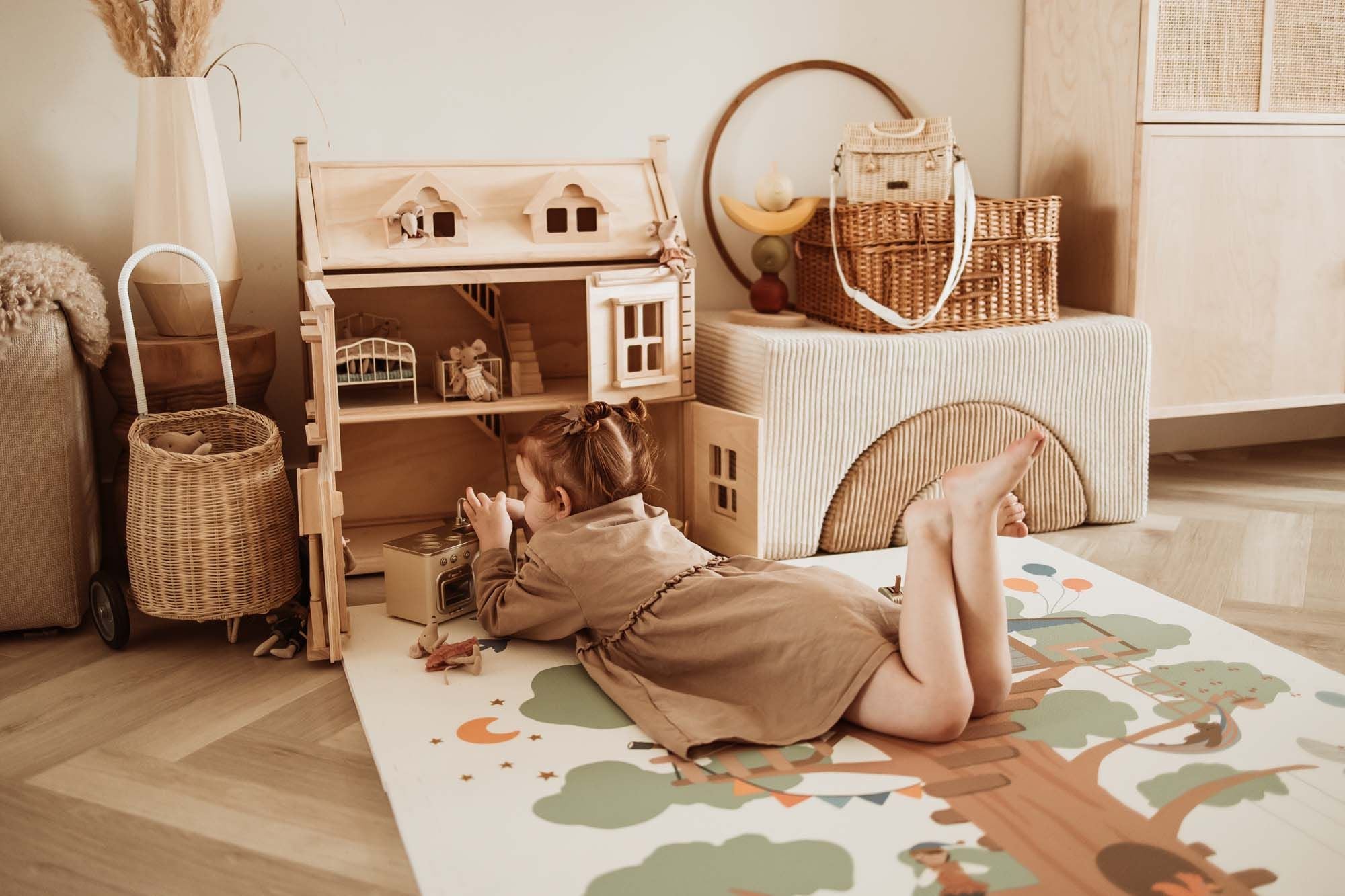 EEVAA treehouse puzzlemat, child is lying on the mat while playing with toys and the wooden victorian playhouse