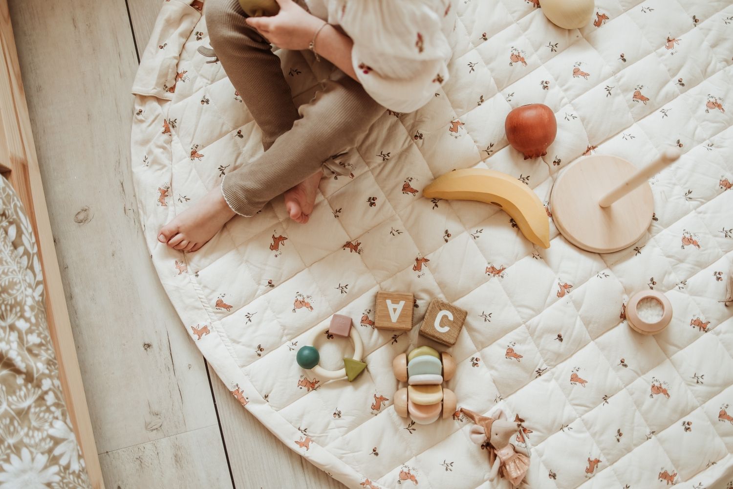 rabbit soft organic babymat, open on floor, child is sitting on the mat while playing with wooden toys