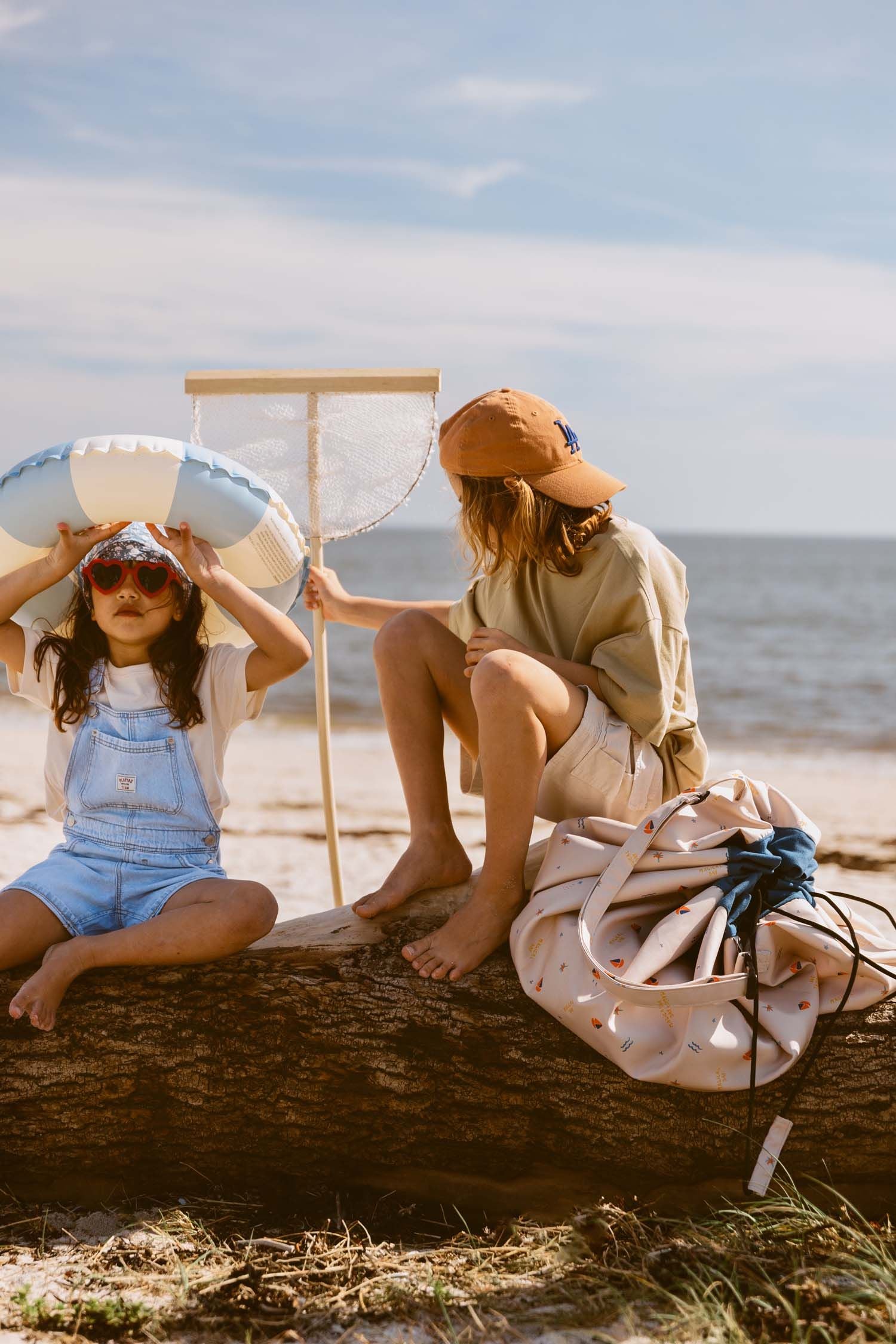 magical days outdoor beach bag, children are sitting on a fallen tree at the beach, holding a swimming band and a fishing net, closed bag