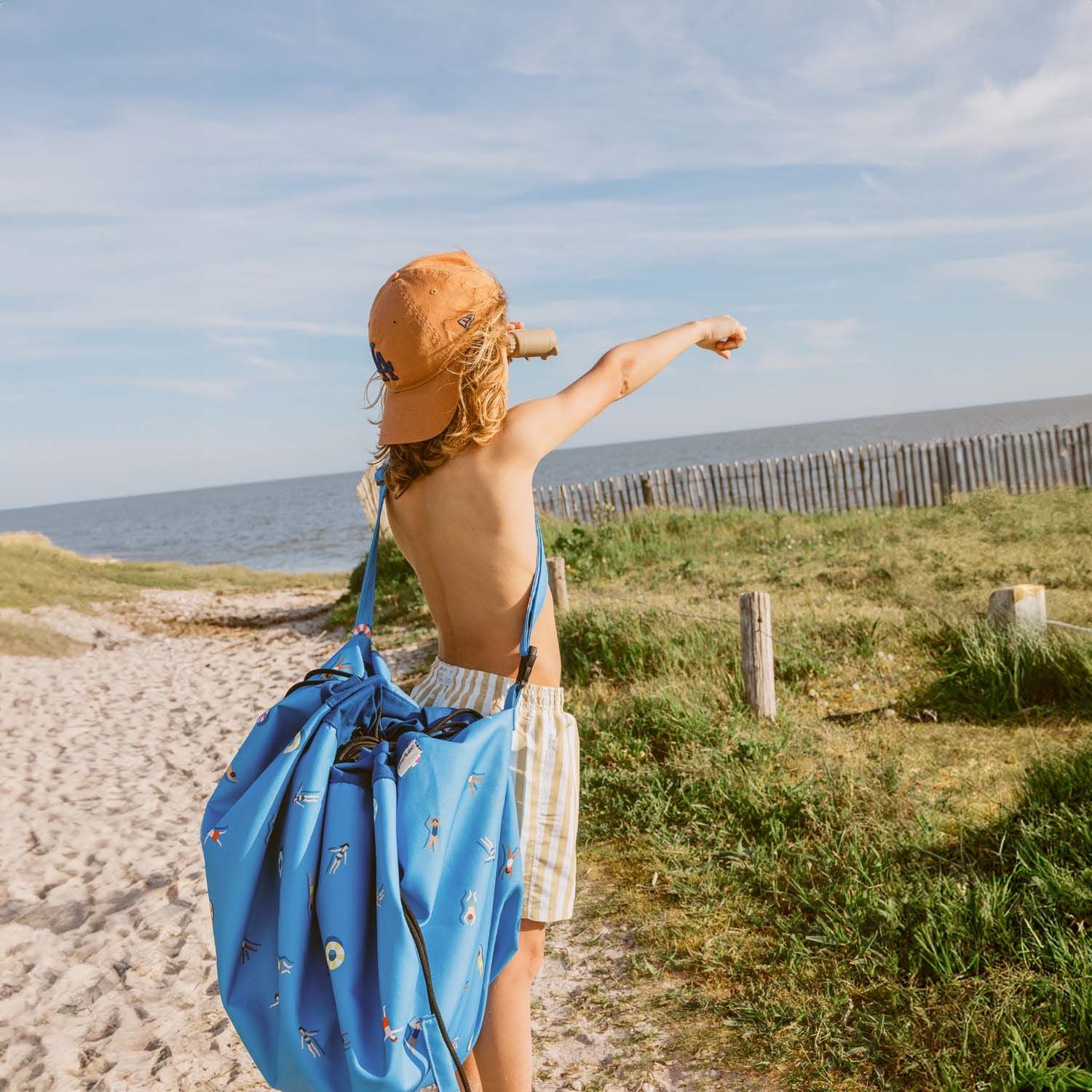 swim fun outdoor beach bag, child is carrying the bag at his shoulder with a shoulder strap, looking far away