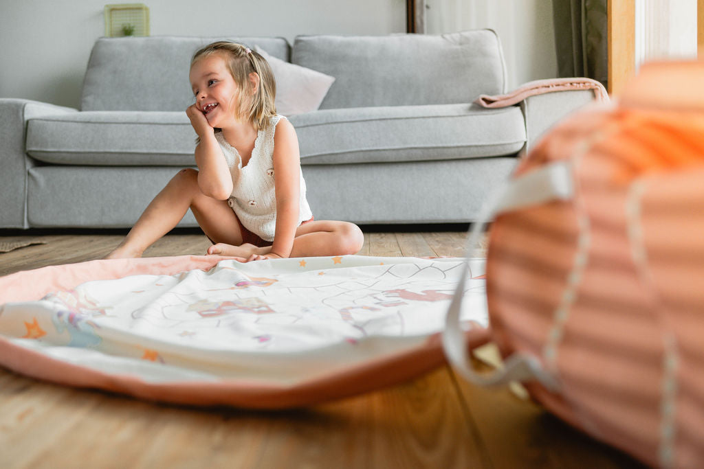 soo fairyworld, open basket with playmat on the floor, sofa in the background, child is sitting next to the mat, dreaming and smiling