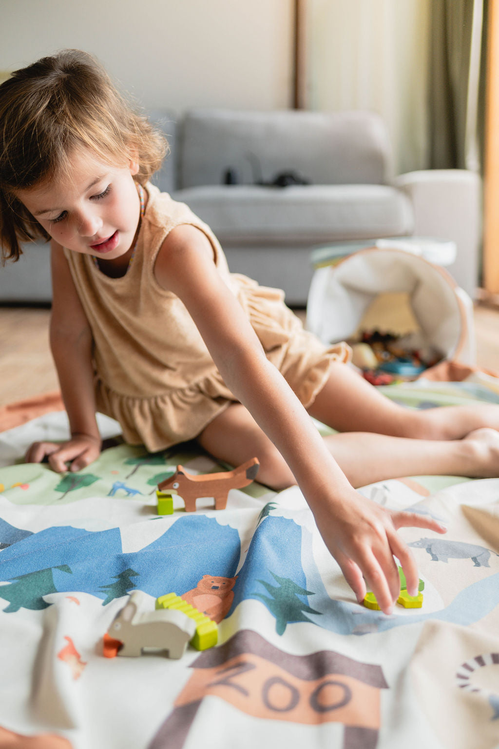soo zoo, open basket and open mat with lots of toys, child is sitting on the mat while playing with wooden toys