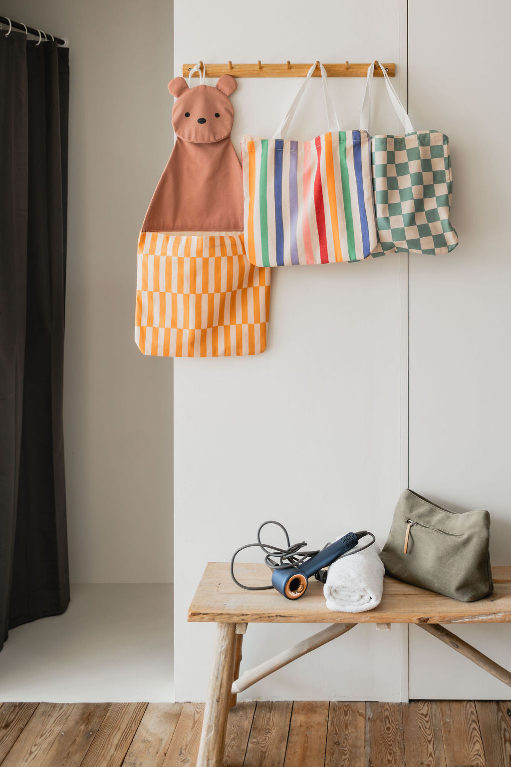 toto bear, hanging on a coat rack, toto unicorn and toto dino transformed into bags, hair dryer, towel and toiletry bag on wooden bench