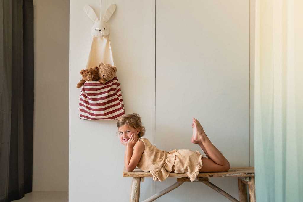 toto bunny, hanging on wall, filled with cuddles, child is laying on a wooden bench, looking into the camera
