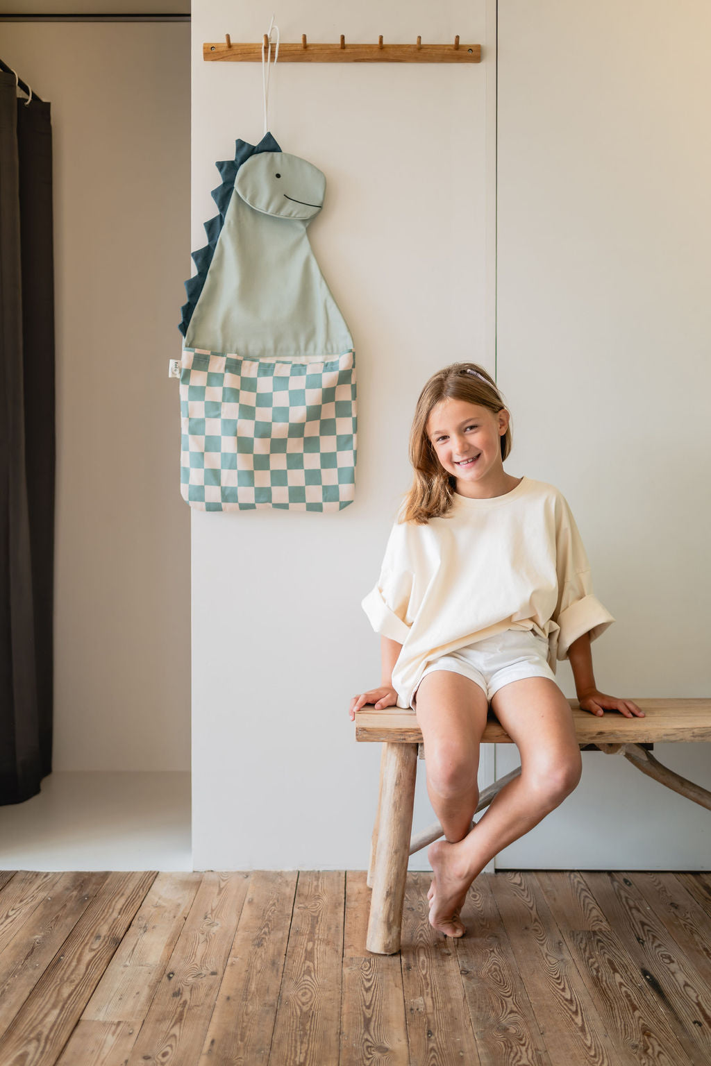 toto dino, hanging on coat rack, child is sitting on wooden bench in front of the bag