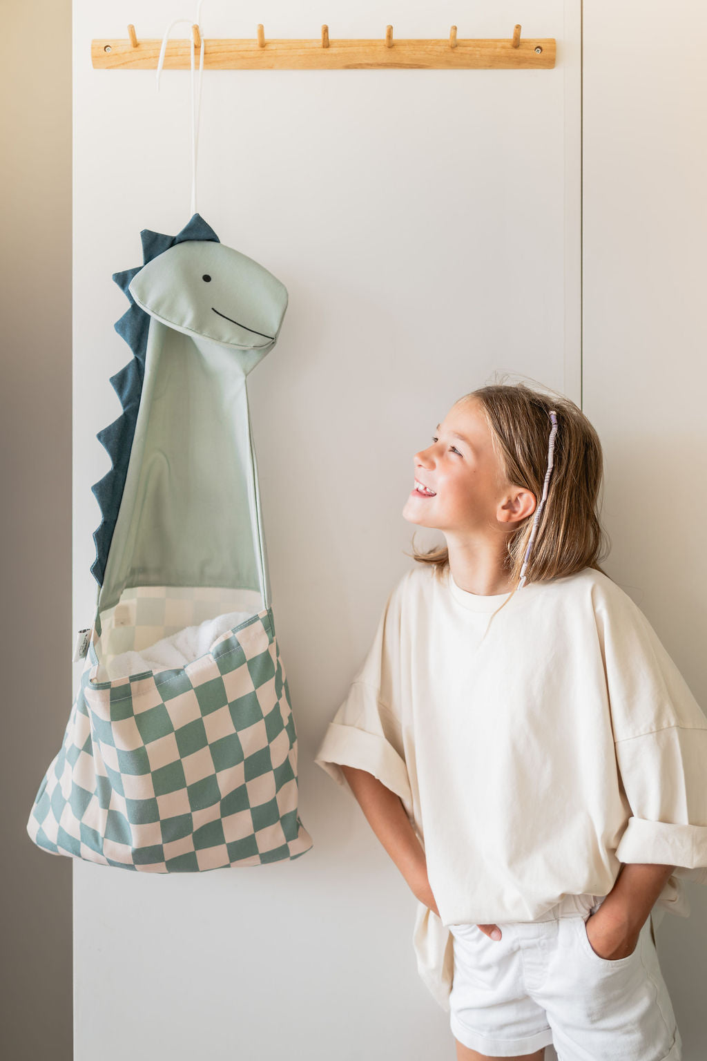 toto dino, hanging on coat rack, filled with towels, child is smiling at the dino