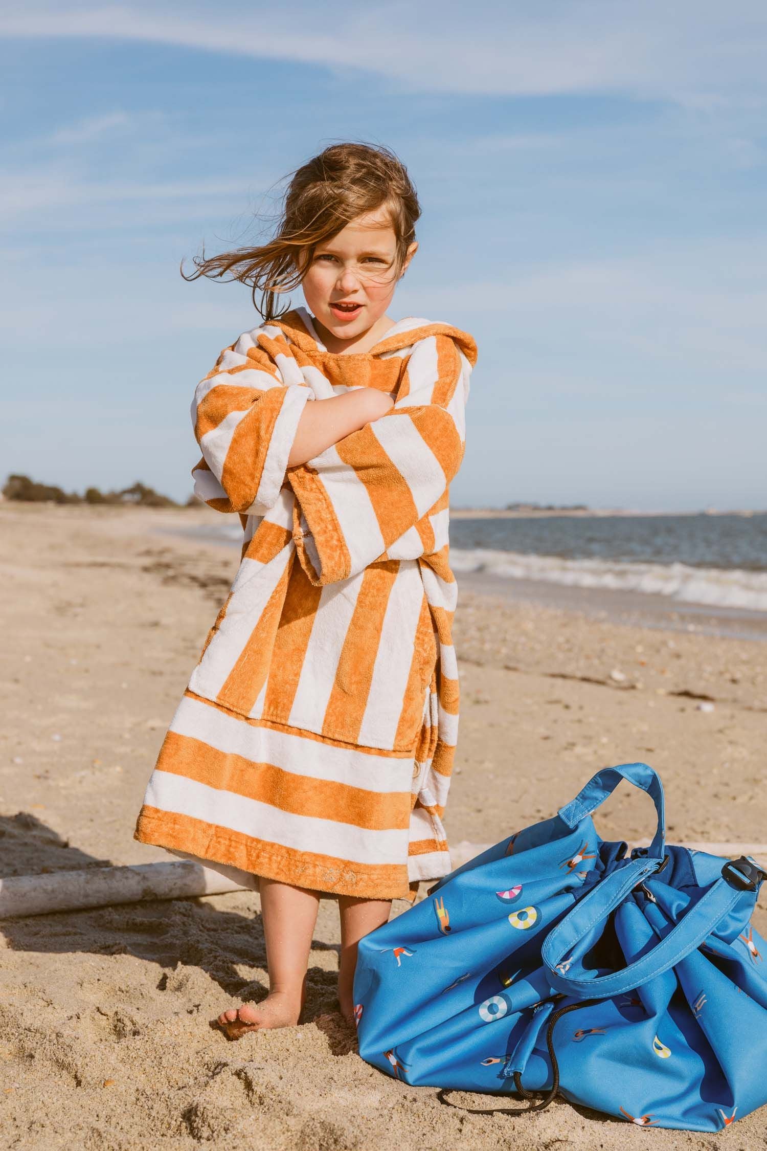 swim fun outdoor beach bag, child is standing in the sand, covered in a towel, standing next to the bag