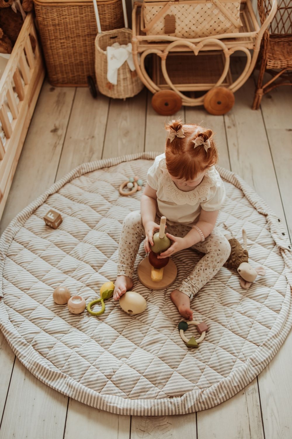soft stripes blue organic babymat, child is sitting on the mat, playing with wooden toys, kidsroom, baskets and a bed