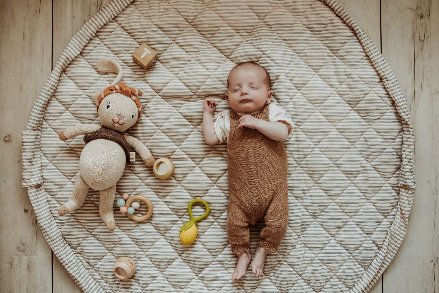 soft stripes blue organic babymat, little baby is sleeping on the open bag, wooden toys and a soft cuddle