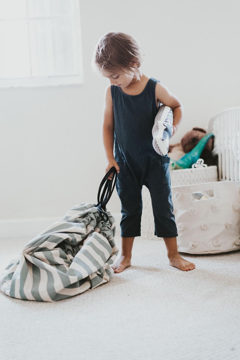 toy storage bag and play mat, green stripes, child carrying the bag and cuddle in the other hand