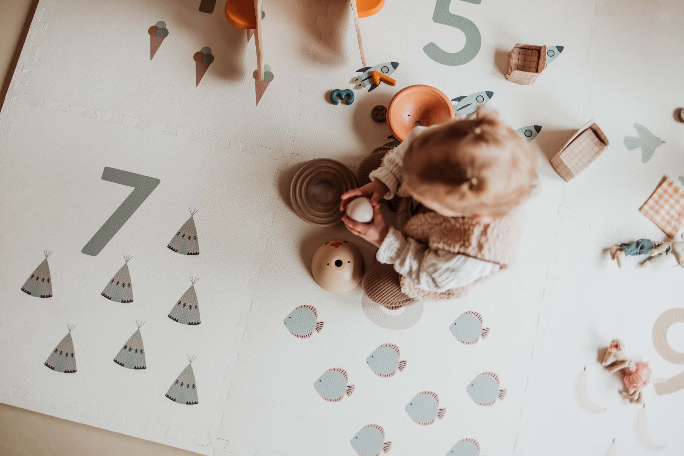 child sitting on numbers puzzlemat, playing with wooden toys
