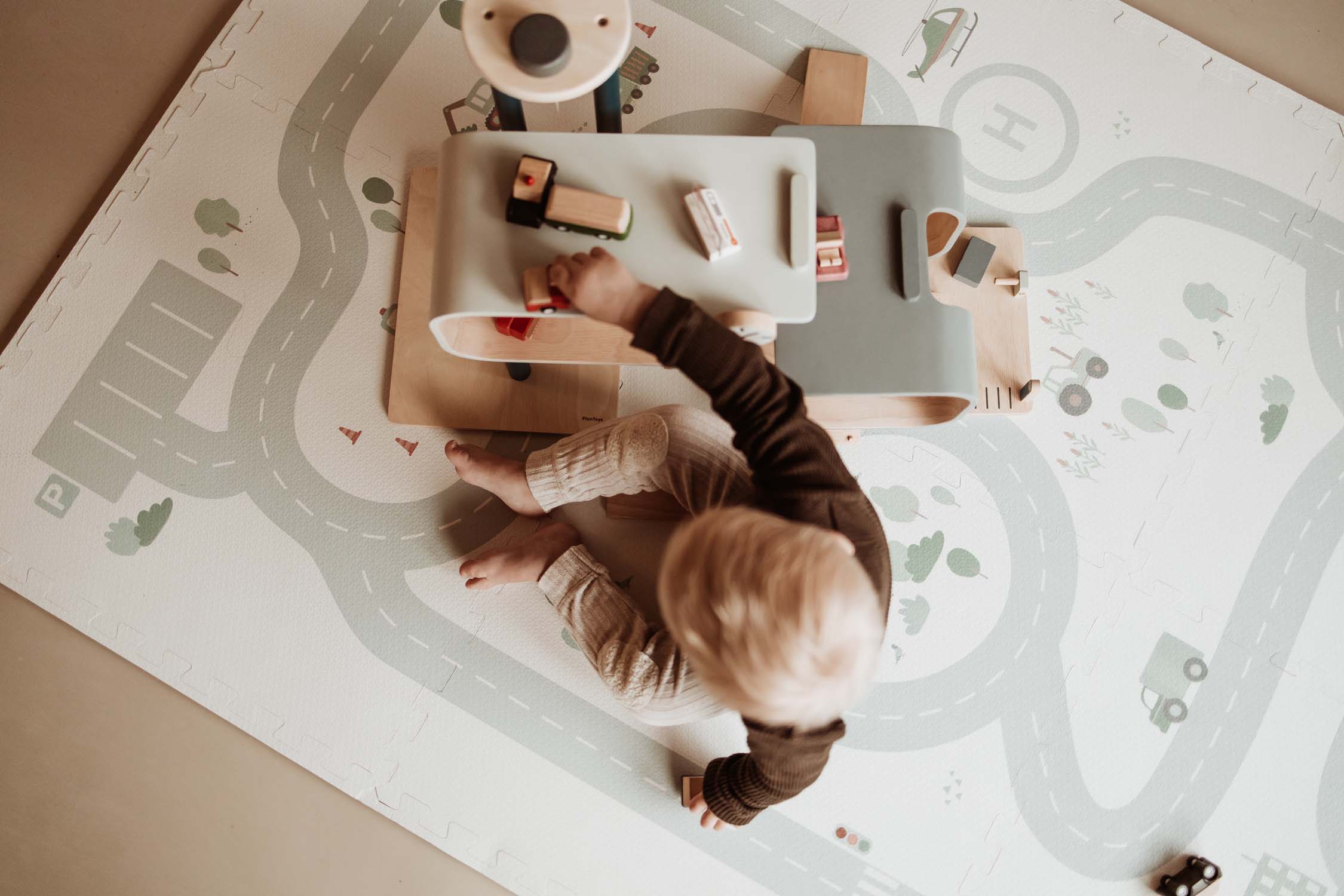 child playing with wooden garage and toys on roadmap puzzlemat