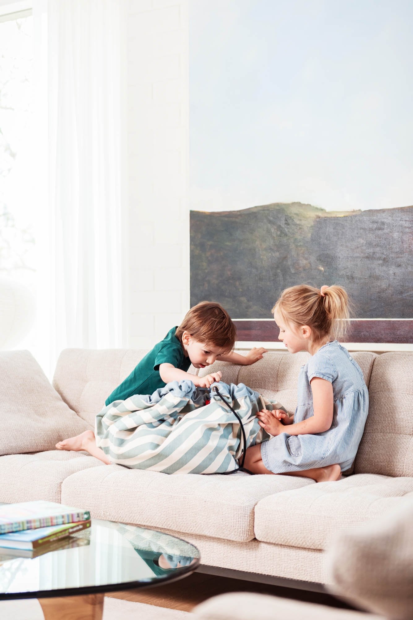 toy storage bag and play mat, kids sitting in sofa, green striped bag between the kids