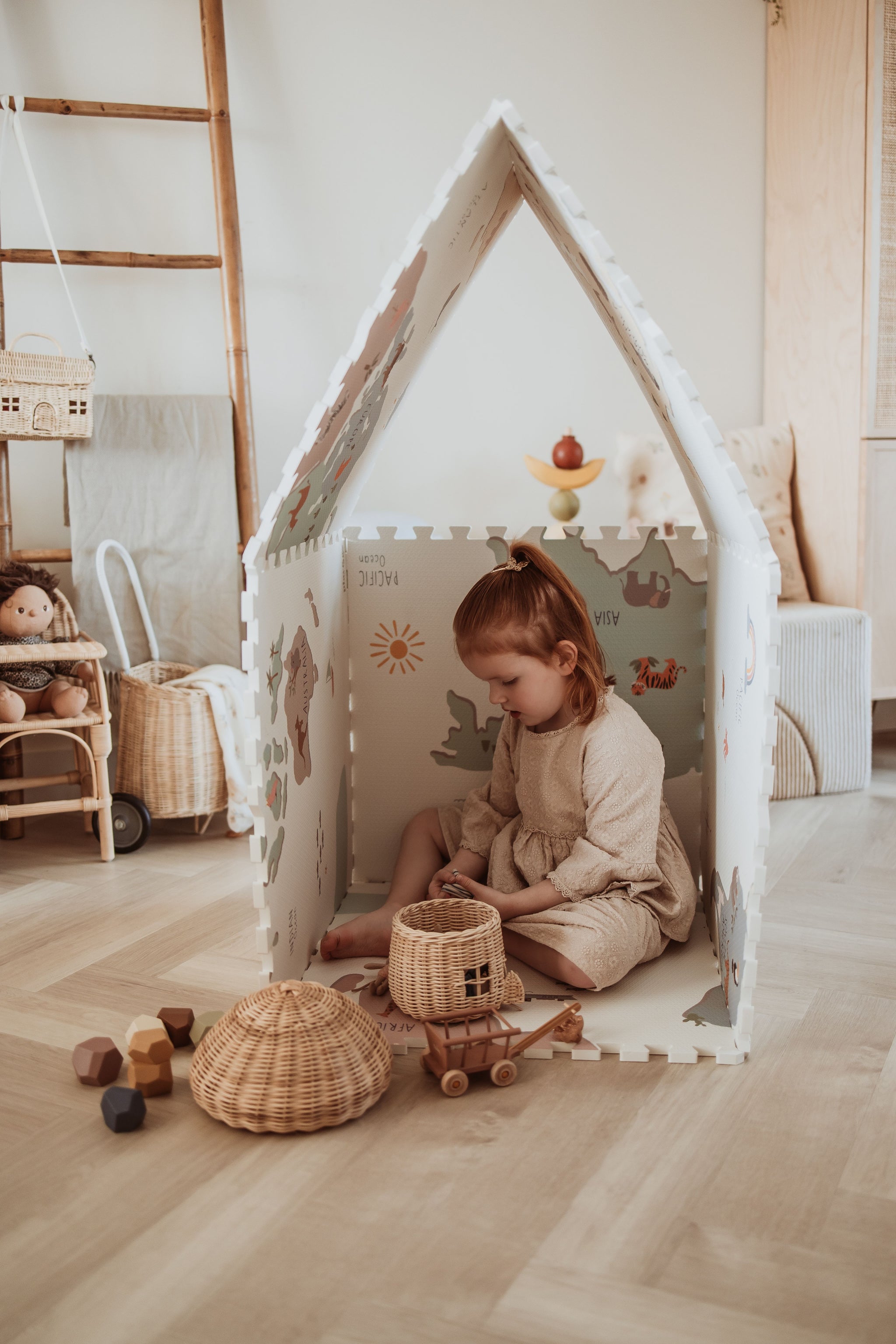 EEVAA worldmap puzzlemat, playhouse, child is sitting in the house playing with wooden basket and wooden toys