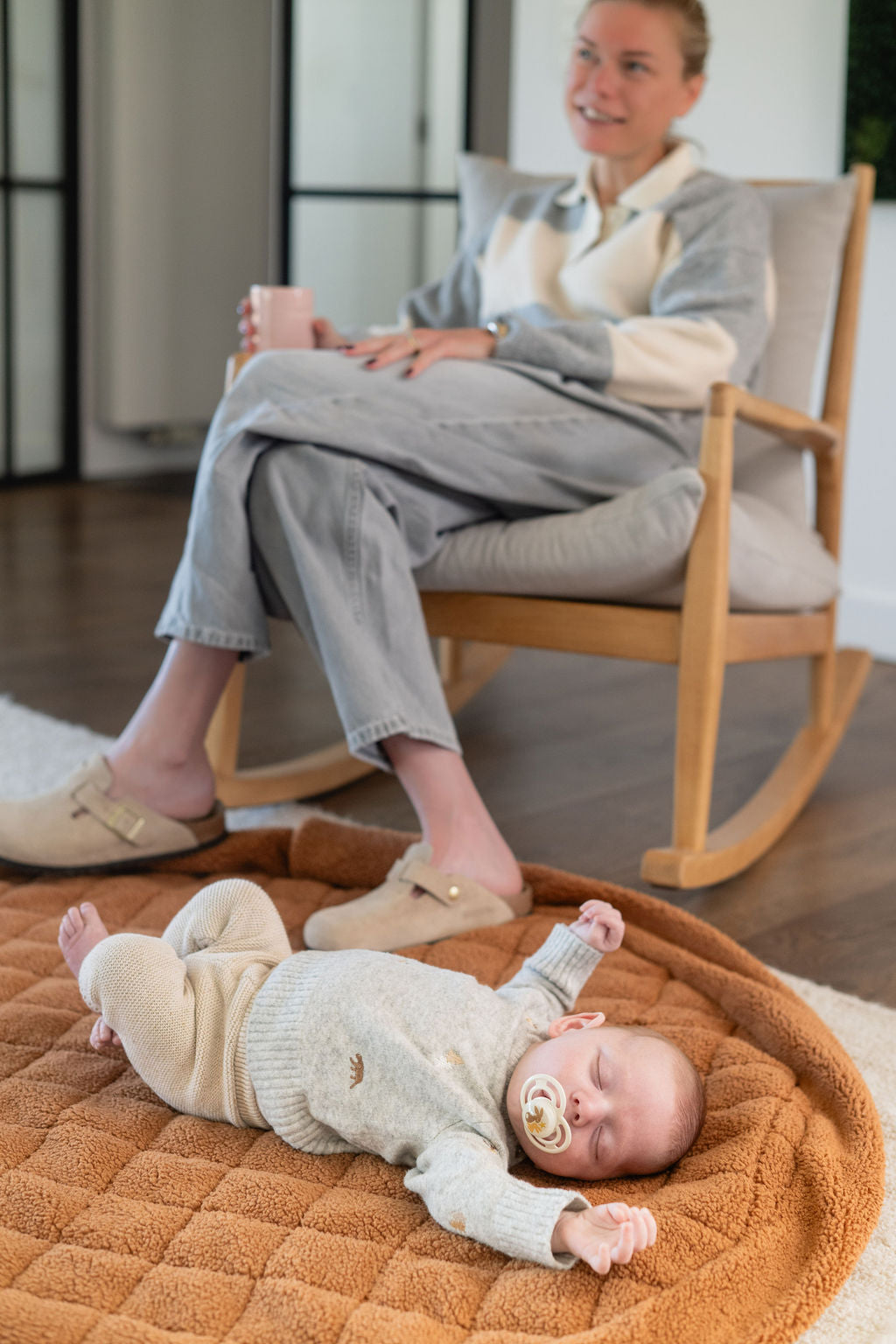 noomad soft teddy brown, person is sitting next to the open mat on the floor, baby is sleeping on the mat