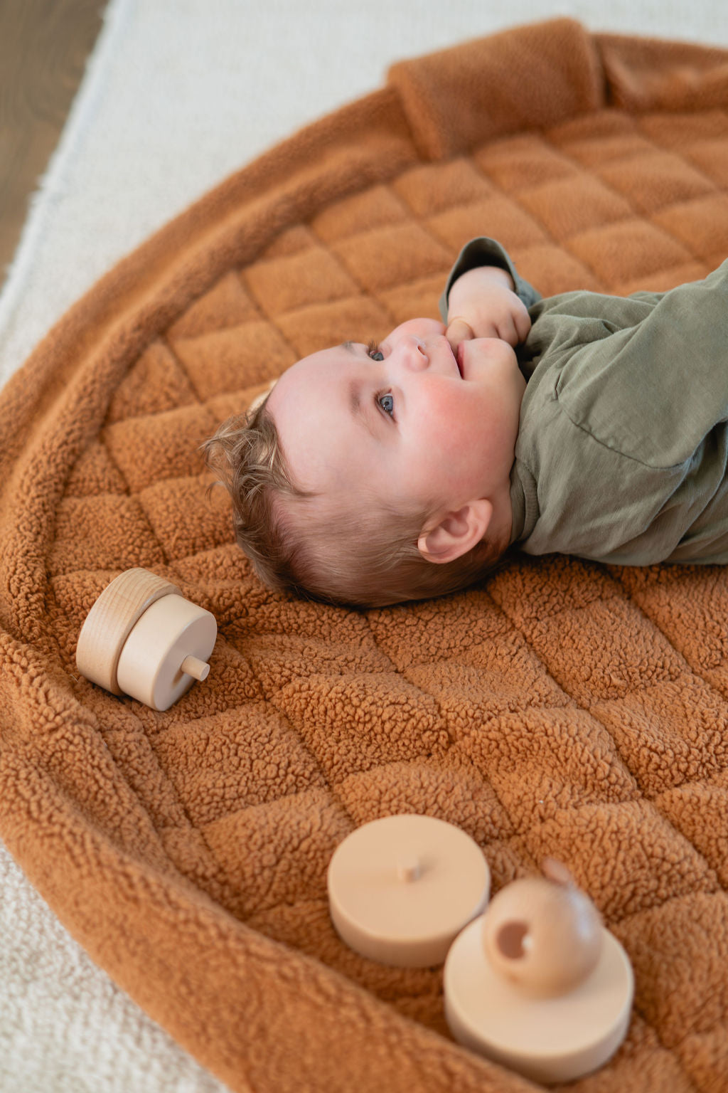noomad soft teddy brown, baby is lying on the open mat, laughing, wooden cuddles