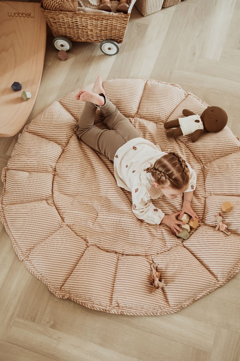 bloom stripes brown babymat, open on floor in kidsroom, child in lying on the mat, playing with wooden toys
