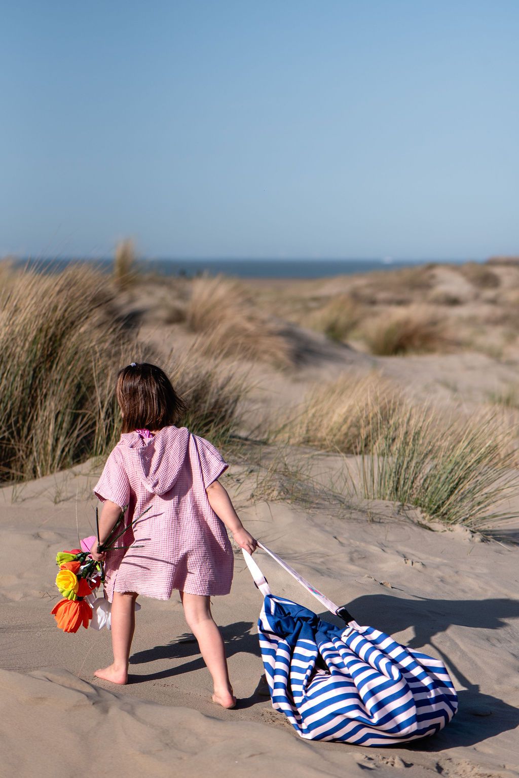 Beach outdoor storage bag, child in a pink dress walking on a sandy beach with a striped bag.