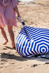 Beach outdoor storage bag, person in a pink dress with a blue and white striped beach bag on a sandy beach.