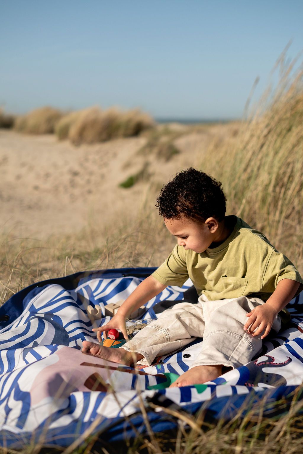 pirate outdoor playmat, child playing on a playmat in a natural setting with sand and grass.