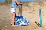 pirate outdoor playmat, child standing on a sandy beach with a blue and white patterned bag, pulling on the ropes