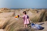 Beach outdoor storage bag, child in a pink dress holding flowers on a sandy beach with dunes and blue sky.