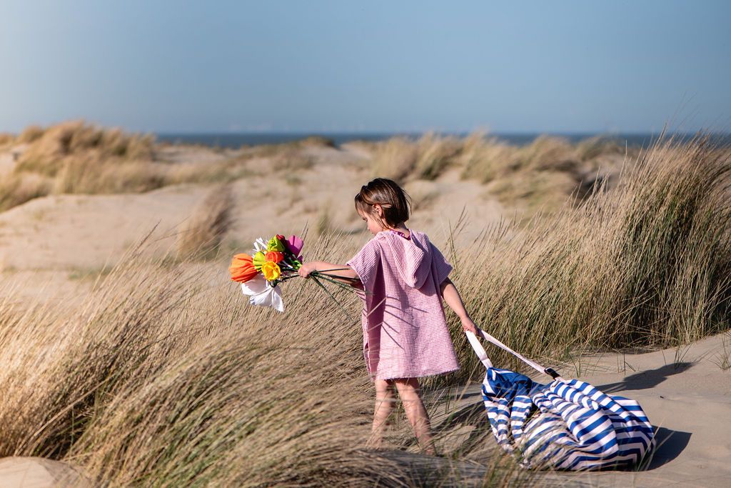 Beach outdoor storage bag, child in a pink dress holding flowers on a sandy beach with dunes and blue sky.