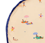 Beach outdoor storage bag, illustration of people at the beach with towels, umbrellas, and a volleyball net on a beige background.