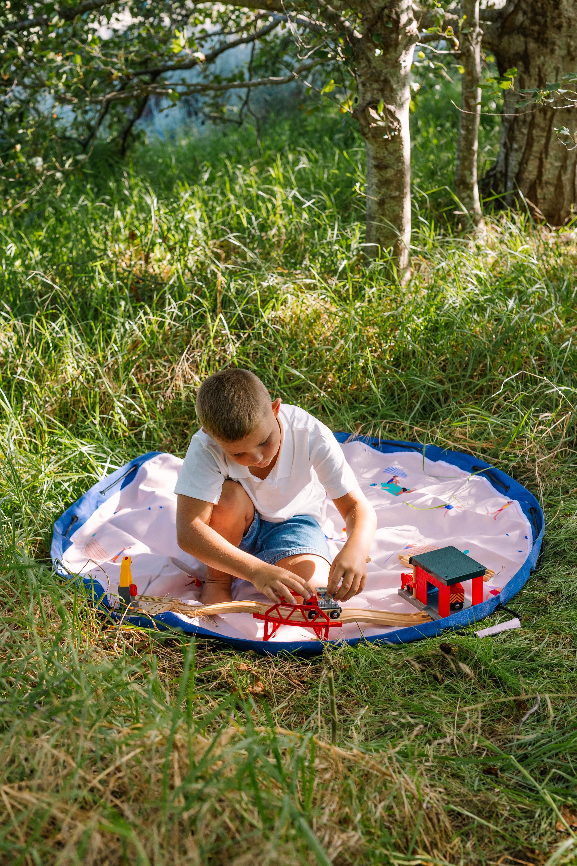 Beach outdoor storage bag, a child is sitting on the open mat in the garden, playing with a toy bridge