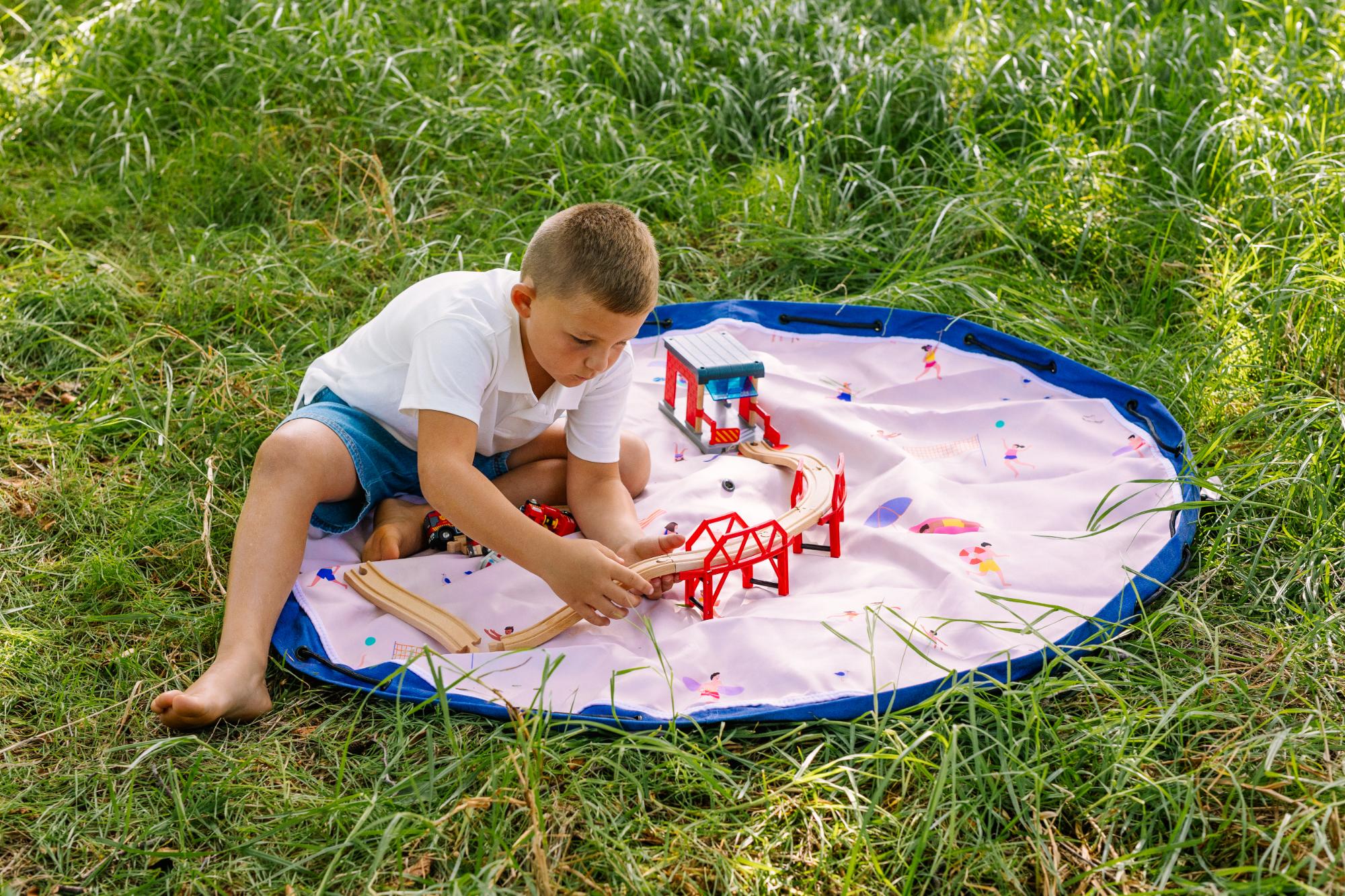 Beach outdoor storage bag, child is sitting on the open mat in the garden ,playing with a bridge construction