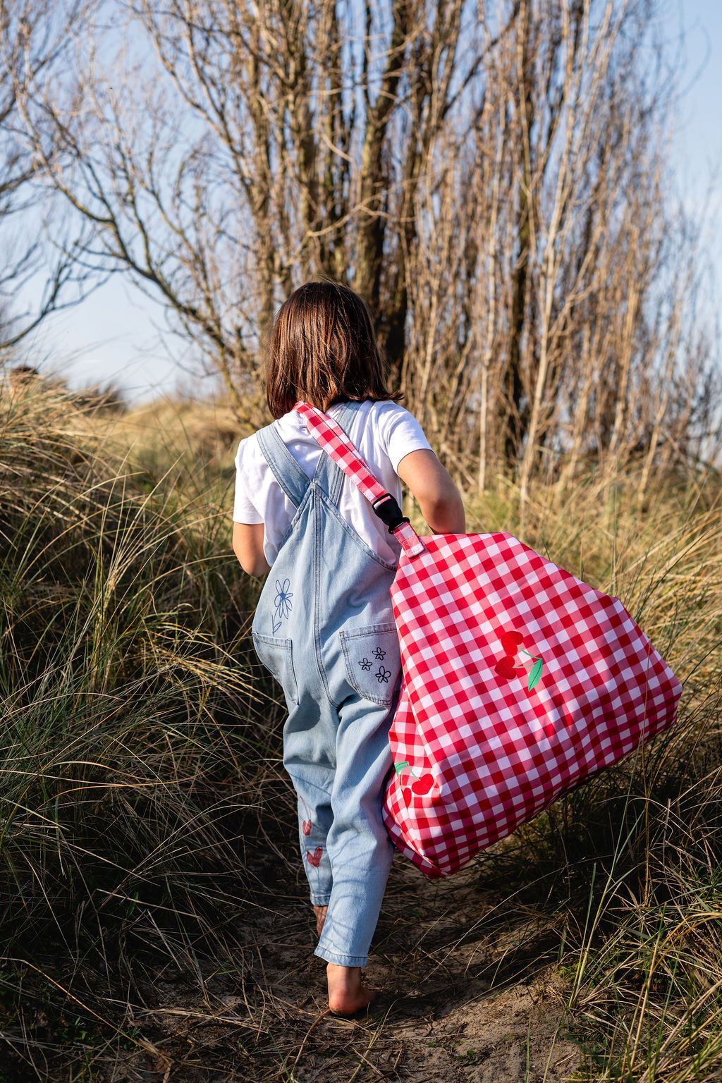pic nic outdoor playmat, child is walking between dune grass while carrying the outdoor bag on its shoulder