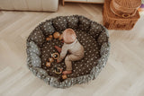 bloom birds babymat, crib, raised edges, child is sitting in the crib, wooden toys and a doll