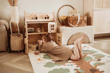 EEVAA treehouse puzzlemat, child is lying on the mat while playing with toys and the wooden victorian playhouse
