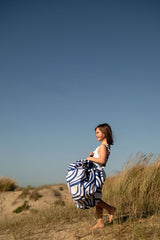pirate outdoor playmat, child in a blue and white swimsuit standing in a field of dunegrass with a clear blue sky, carrying the bag