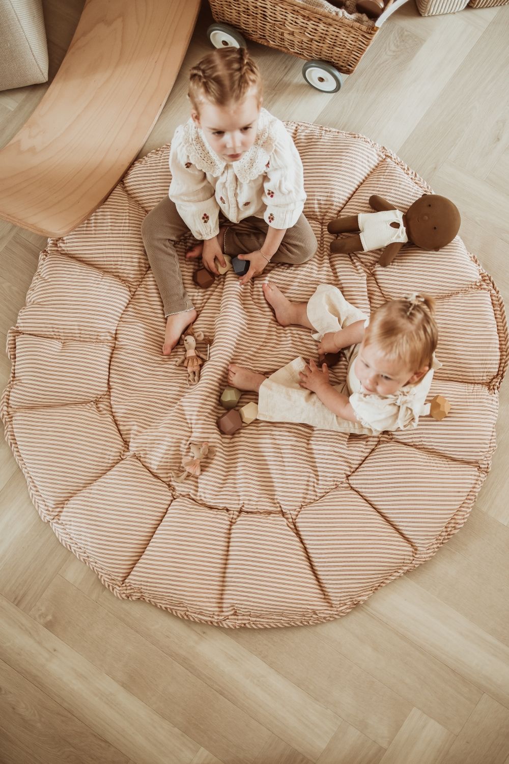 bloom stripes brown babymat, open on floor, in kidsroom, children are sitting on the mat, wooden toys and dolls, wooden slide