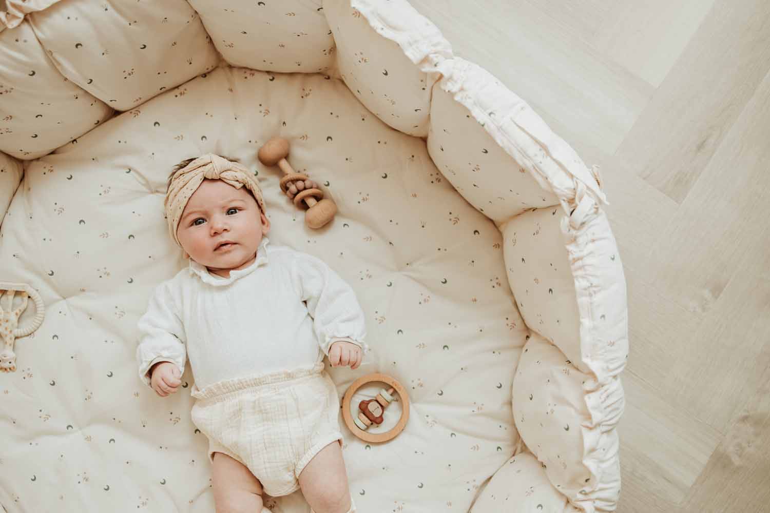 Bloom Moon organic babymat, baby lying in crib with raised edges and wooden toys