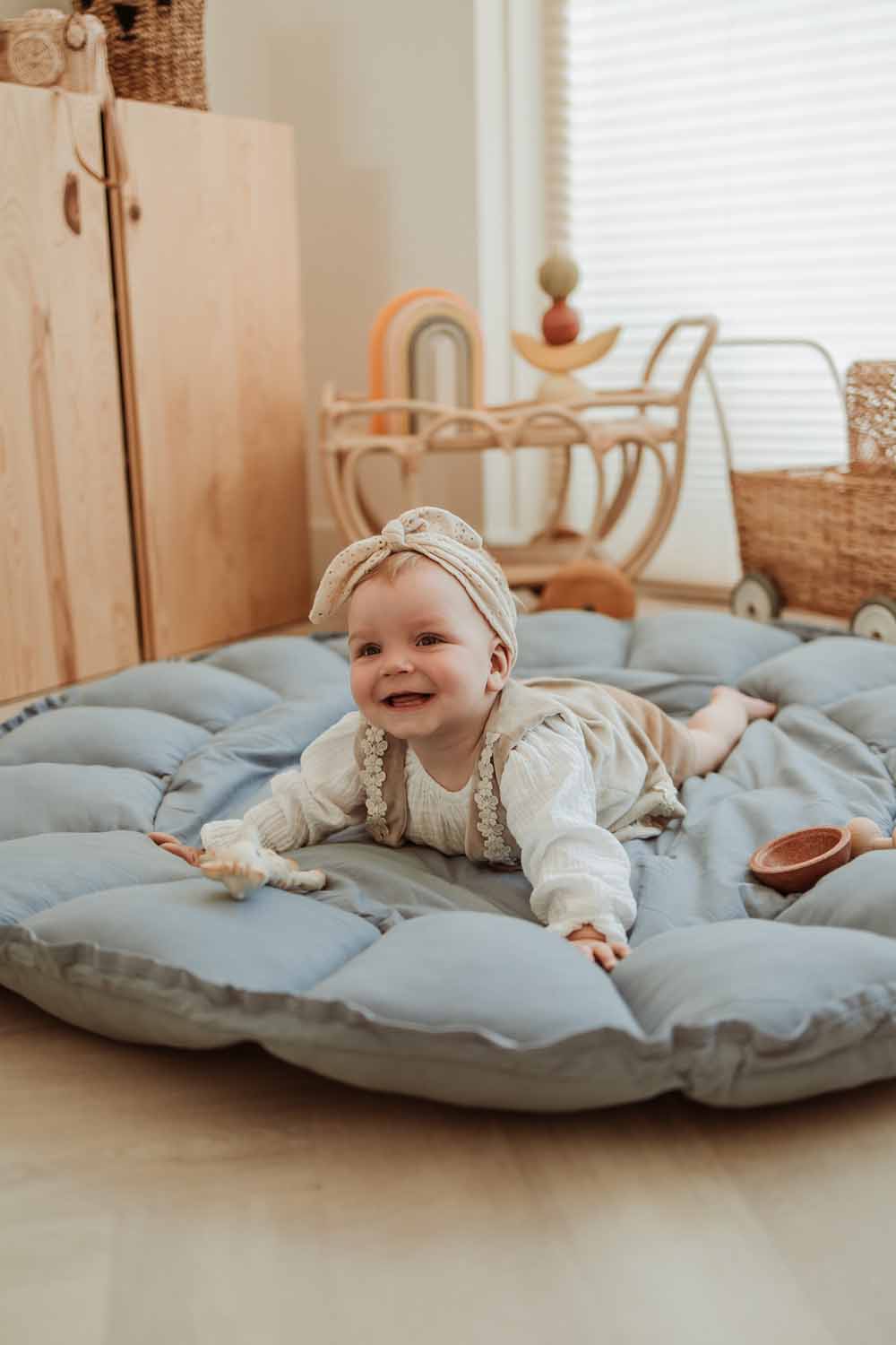 Bloom dusty blue organic babymat, child lying down on the mat, laughing and playing, wicker baby carriage                                