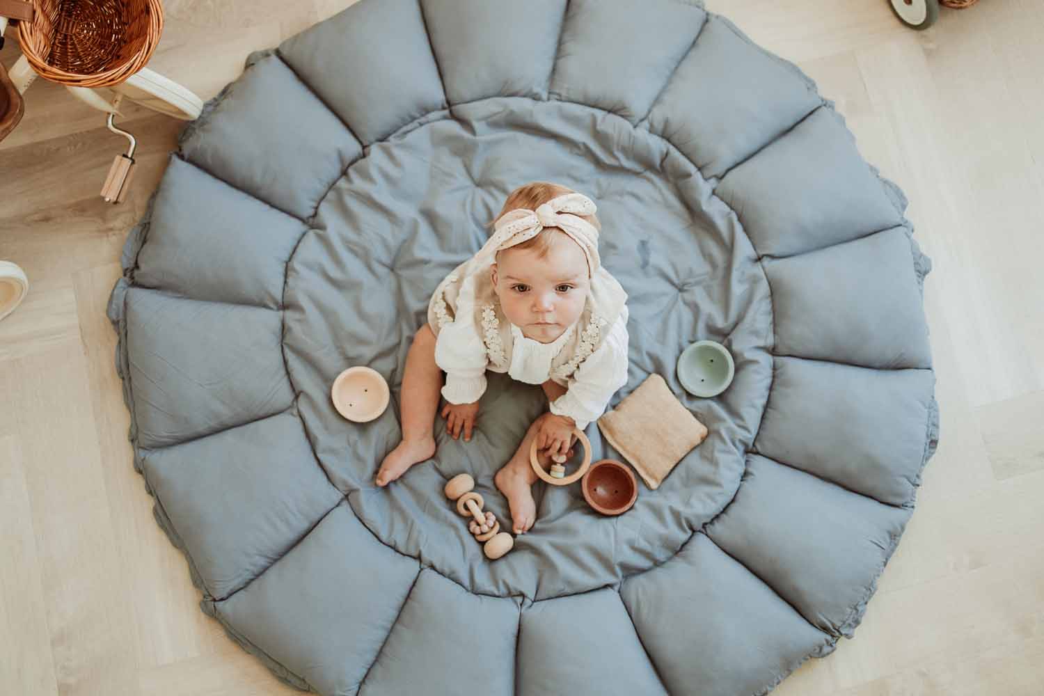 Bloom dusty blue organic babymat, open on floor, little child sitting on the mat, playing with toys and looking up