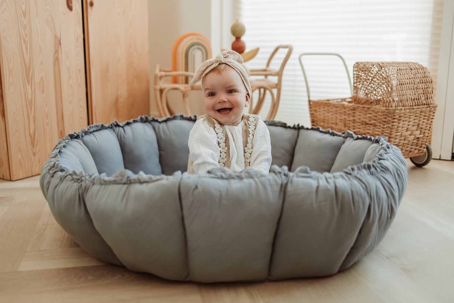 Bloom dusty blue organic babymat, raised edges, little child sitting on mat, laughing, wicker baby carriage