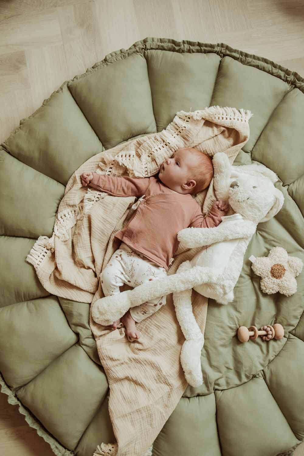 Bloom meadow green organic babymat, little baby lying on open mat on blanket, next to soft cuddle