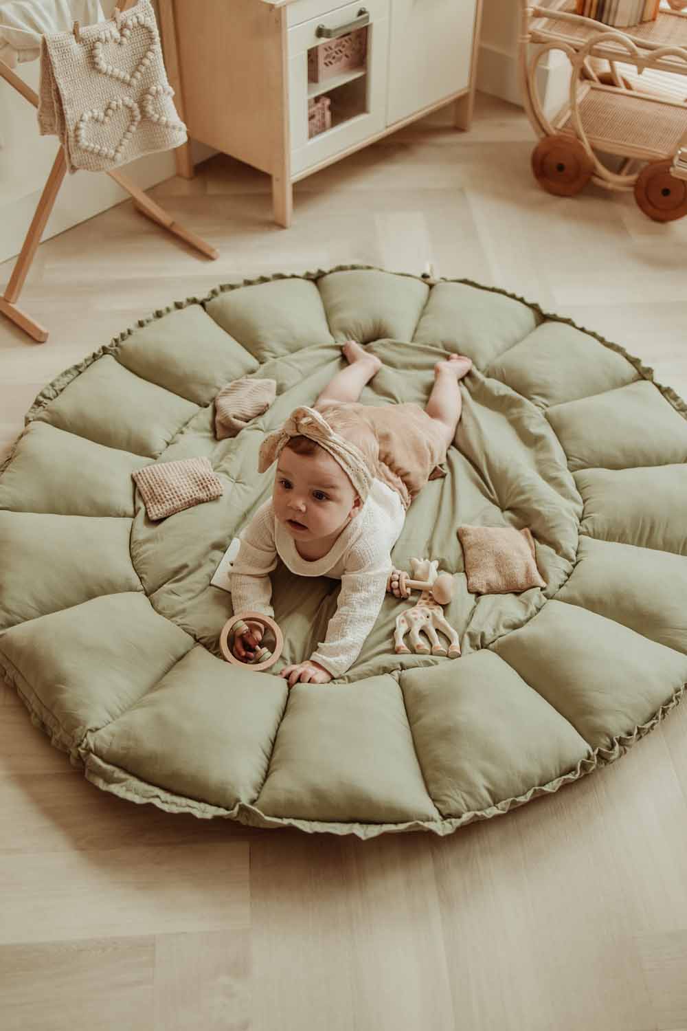 Bloom meadow green organic babymat, child lying on open mat on floor in kidsroom, next to wooden kitchen