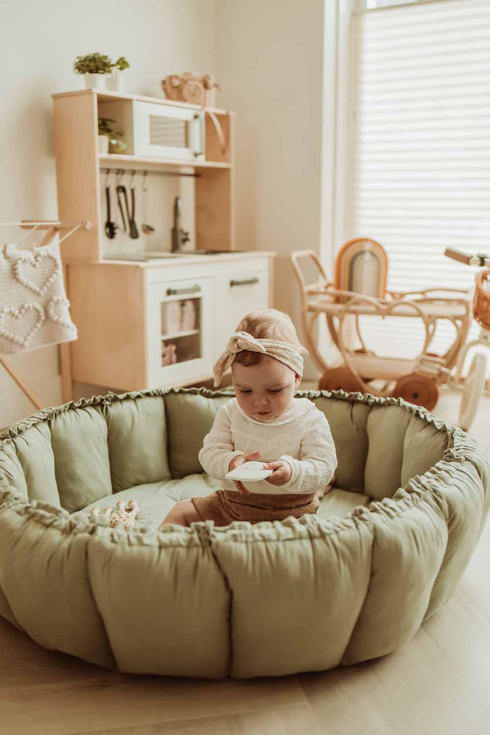 Bloom meadow green organic babymat, raised edges, baby sitting on mat in kidsroom, wooden kitchen