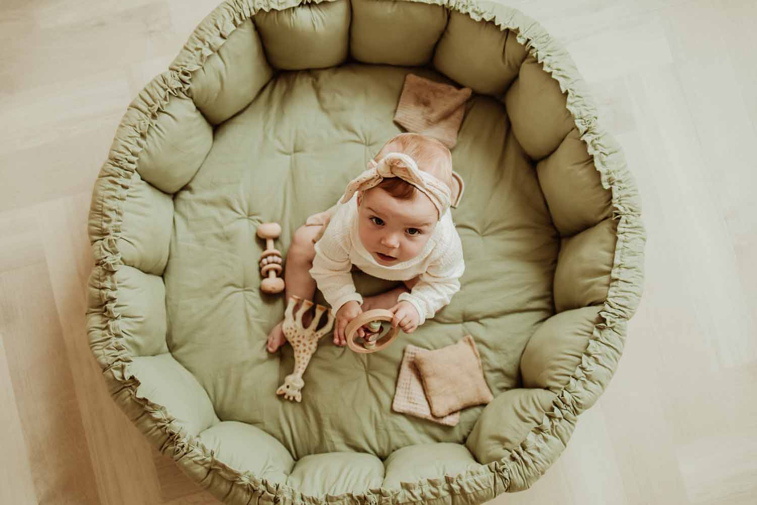 Bloom meadow green organic babymat, raised edges, child sitting on mat between toys, looking up