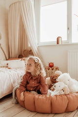 Bloom tawny brown organic babymat, raised edges, child sitting on mat between cuddles, next to bed in kidsroom