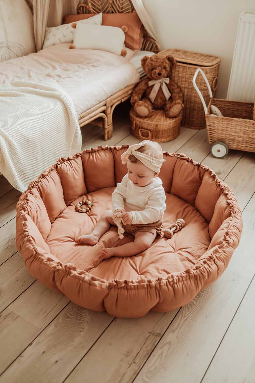 Bloom tawny brown organic babymat, raised edges, little child sitting on mat on floor in kidsroom next to bed, cuddle bear and baby carriage