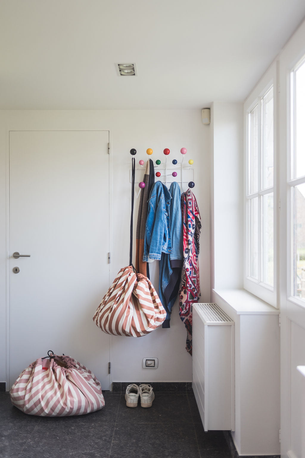 Stripes brown toy storage bag and play mat, hanging on coat rack next to jackets, stripes pink storage bag closed on floor