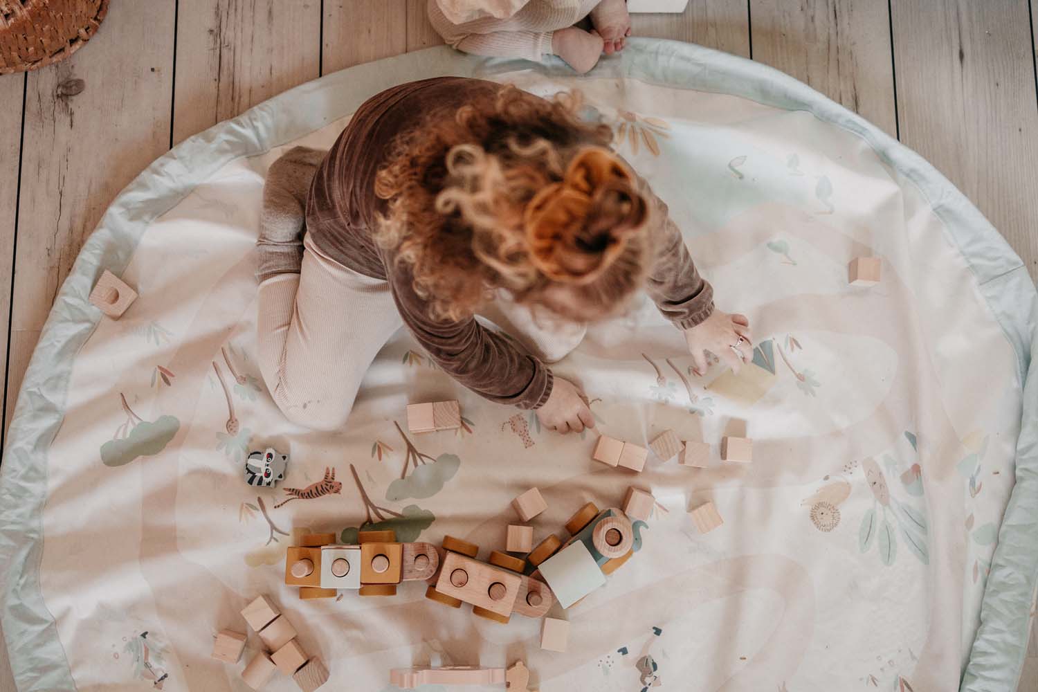 jungle storage bag, child playing on open mat on floor, wooden toys and wooden train