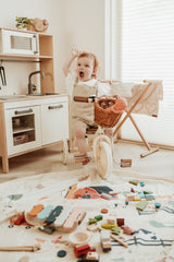 farm toy storage bag and play mat, child riding on tricycle and waving, lots of wooden toys and wooden play kitchen
